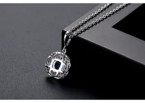 Primer plano de un colgante redondo plateado con calados de corazón y una piedra de circón azul.