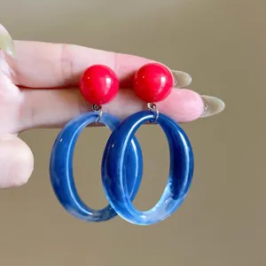 Detailed view of vibrant dopamine-style red stud earrings with blue resin oval drops