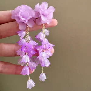 Close-up of elegant purple flower tassel earrings featuring matte petals and gold chains.