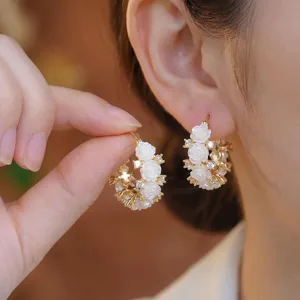Close-up of elegant gold hoop earrings with white resin roses and sparkling crystals