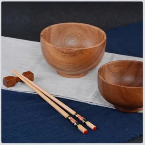 Handcrafted acacia wood bowl set with floral chopsticks on a rustic fabric background