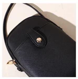Macro detail shot showing the textured black leather and gold snap button of the phone bag