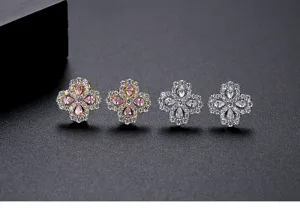 Close-up view of four sparkling clover flower stud earrings with pink and clear stones.