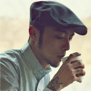 Detalle de una gorra plana retro gris para hombre usada por un modelo en una escena de café