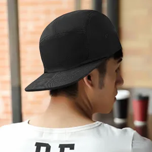 Stylish black five-panel flat brim camper hat worn by a model in a street setting