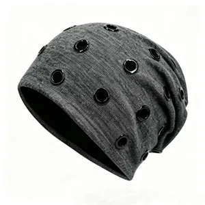 Detail view of grey slouchy beanie hat featuring multiple black metal grommets for a punk hip-hop style