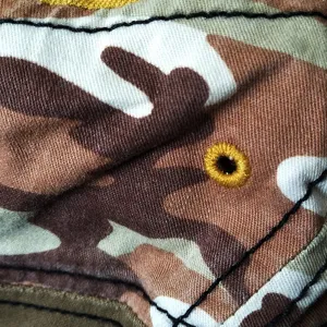 Macro detail of camouflage cotton military cap showing yellow embroidered eyelet