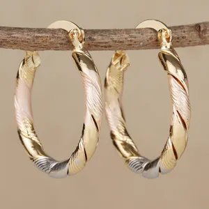 Detailweergave van driekleurige gedraaide oorringen met goud, zilver en roségoud finish