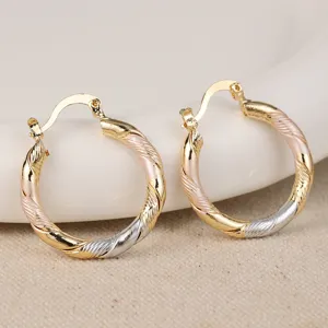 Detailopname van driekleurige gedraaide oorringen in goud, zilver en roségoud