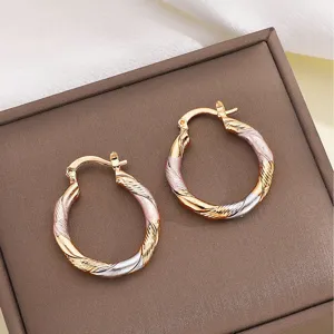 Detailopname van driekleurige gedraaide oorringen met goud, zilver en roségoud finish