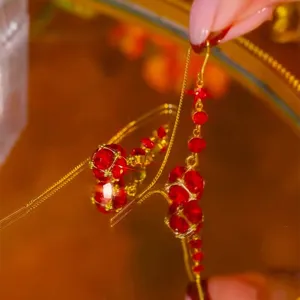 Close-up macro view of red crystal petal tassel earrings on a golden mirror surface