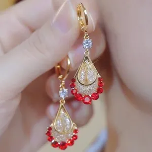 Detailed close-up of gold-tone teardrop earrings featuring red crystals and pave-set stones