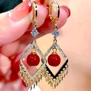 Detailed close-up of gold tassel earrings featuring vibrant red beads and rhinestones