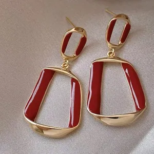 Close-up of elegant gold-toned geometric earrings with deep red enamel finish.