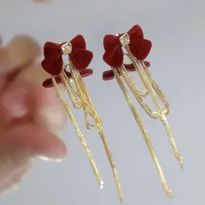 Detail view of elegant deep red velvet bow earrings featuring long gold chain tassels
