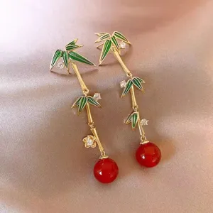 Macro detail of elegant bamboo tassel earrings with green enamel and red beads