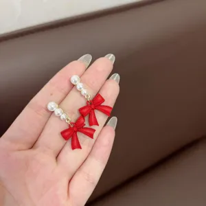 Primer plano de elegantes pendientes de lazo rojo con perlas blancas en una mano