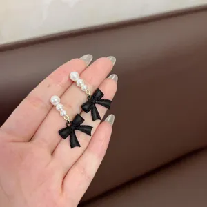 Detalle de los elegantes pendientes de lazo negro con delicadas perlas blancas finas.