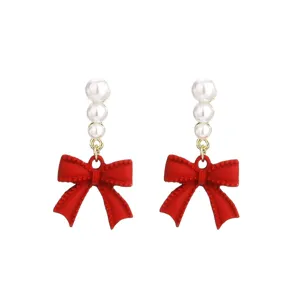 Primer plano de elegantes pendientes de lazo rojo con tres perlas blancas apiladas
