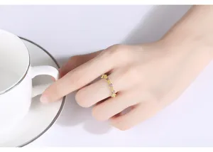 Vista detallada de un elegante anillo dorado con flores de circón rosa en la mano