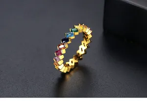Detalle de anillo geométrico dorado con circonitas rectangulares de colores arcoíris.