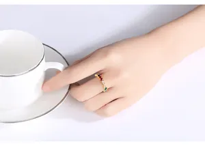 Primer plano de un anillo dorado con circonitas de colores al sostener una taza