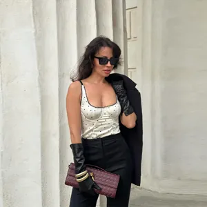 Fashionable white camisole top with black polka dots shown on a model in a chic outdoor setting.