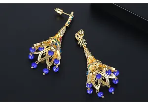Détail de boucles d'oreilles pompons dorées avec zircons colorés et perles de cristal bleu