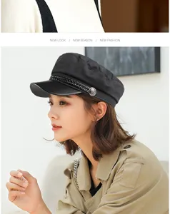 Fashionable black flat-top baker boy cap worn by a model in a beige trench coat