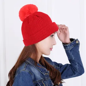 Modella indossa un berretto in maglia rossa invernale con pompon e bordo risvoltato.
