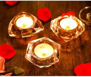 Lot de trois bougeoirs en cristal géométrique avec bougies allumées sur table en bois.
