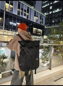Modell mit einem großen schwarzen Roll-Top-Sportrucksack mit Schnallen in der Stadt bei Nacht