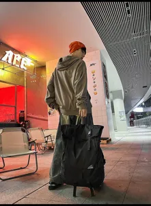 Mann trägt einen großen schwarzen Roll-Top-Sportrucksack in einer urbanen Umgebung.