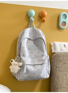 Light grey casual student backpack with heart patterns hanging on a bright yellow wall