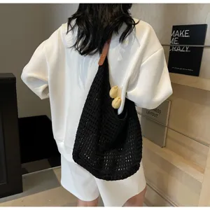 Black hollow-out knitted shoulder bag shown on model's back in a minimalist setting.