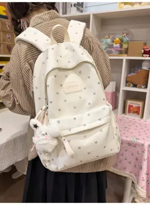 Lifestyle view of white school backpack with heart pattern and plush rabbit charm
