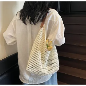 Model wearing a large cream knitted mesh shoulder bag with a brown leather strap