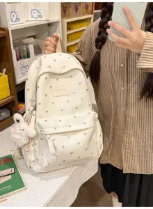 Lifestyle detail of a white heart-pattern backpack with a cute plush charm accessory