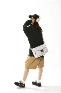 Bolso mensajero funcional techwear en gris claro llevado por modelo sobre fondo blanco