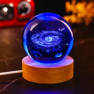 Close-up of glowing 3D laser-engraved galaxy crystal ball night light on wooden base.