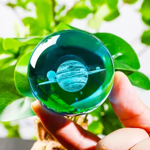 Close-up detail of 3D laser engraved Saturn crystal ball held against green foliage