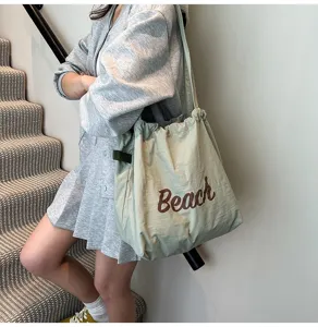 Primer plano de un bolso tote grande verde salvia con estampado 'Beach' en una modelo
