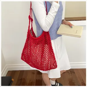 Sac cabas en maille tressée rouge porté par un mannequin, idéal pour les vacances