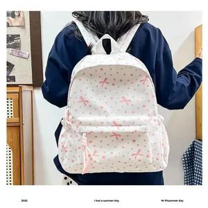 Vista detallada de una mochila escolar blanca con patrones de lazos rosas y flores