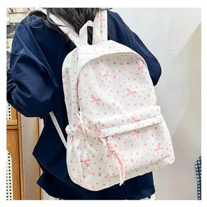 Vista trasera de una mochila escolar blanca con lazos rosas usada por una modelo.