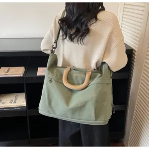 Sage green travel bag with bow embroidery and tan handles in a lifestyle setting