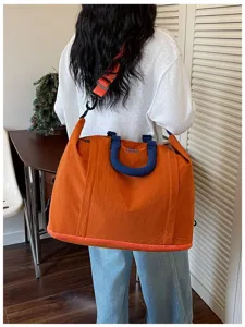 Large orange nylon travel duffel bag with blue handles carried by model for fitness and travel