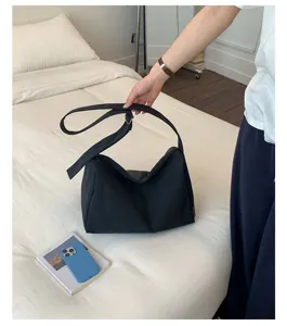 Lässige schwarze wasserdichte Nylon-Umhängetasche, gehalten über einem weißen Bett
