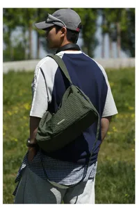 Gros plan d'un grand sac bandoulière vert à carreaux porté par un modèle en plein air
