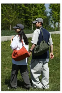 Couple portant de grands sacs à bandoulière de voyage dans un champ vert ensoleillé